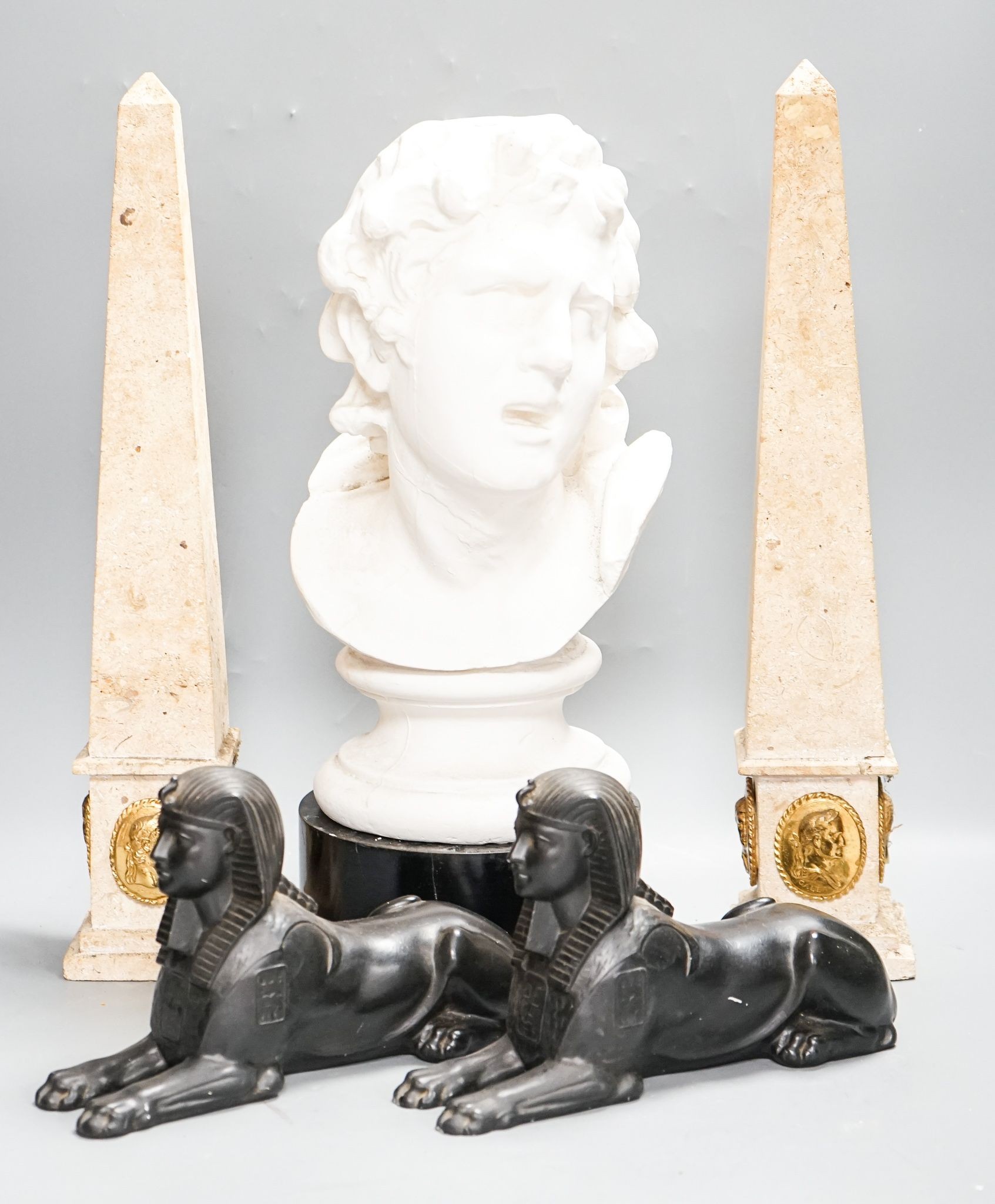 A pair of composition classical faux marble obelisks together with a pair of simulated stone Sphinx, a faux bronze model of Trajan‘s column and a faux marble bust (5)